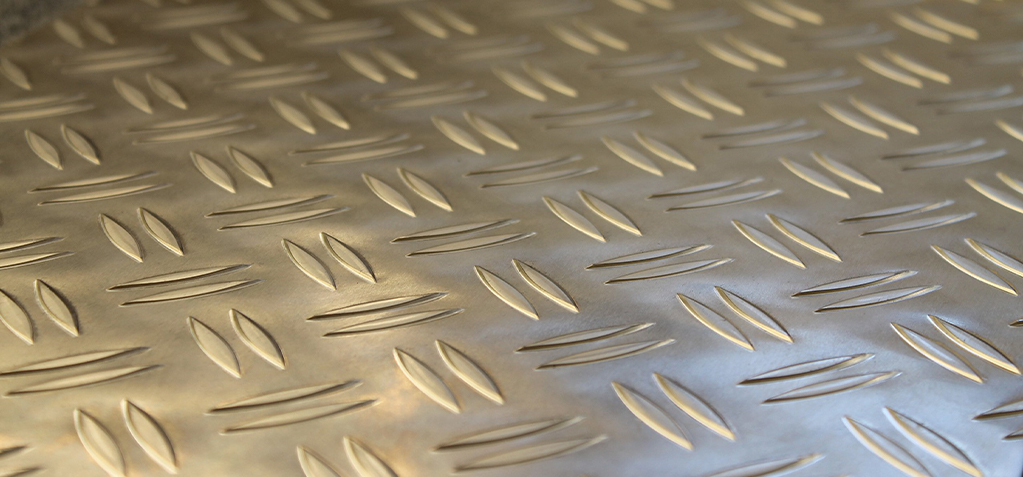 Gros plan d’une tôle aluminium striée aux reliefs allongés avec des reflets dorés et argentés